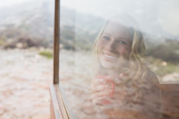 Happy woman with coffee cup looking through window