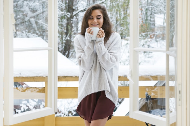 Happy woman with a cup of hot drink on the balcony at winter day