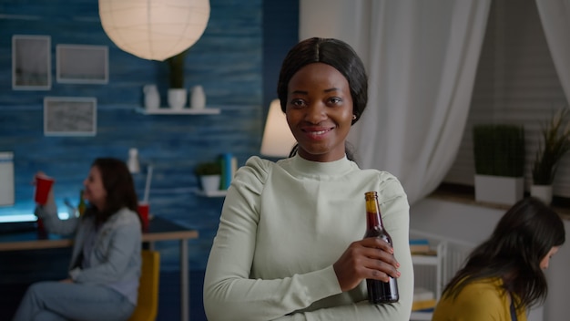 Happy woman with dark skin drinking beer having fun during holiday party