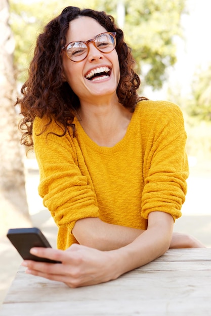 眼鏡をかぶった幸せな女性が携帯電話を握っている