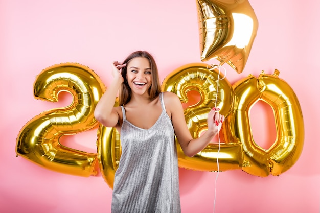 Happy woman with golden new year 2020 balloons isolated over pink