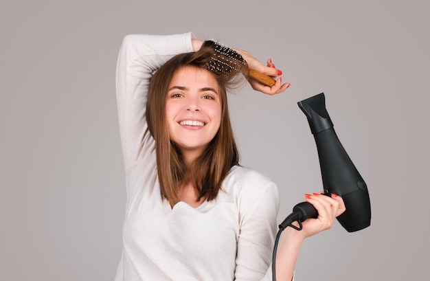 Foto donna felice con l'asciugatrice di capelli ragazza bella con i capelli dritti asciugando i capelli con un asciugatore di capelli professionale