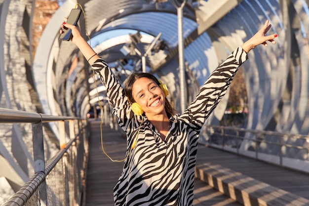 Happy woman with headphones having fun at the city while listening music