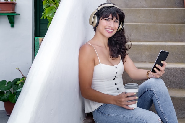 Happy woman with headset using the smartphone on the steps