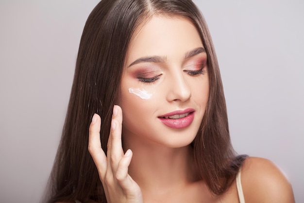 Happy woman with healthy face applying cream under the eyes