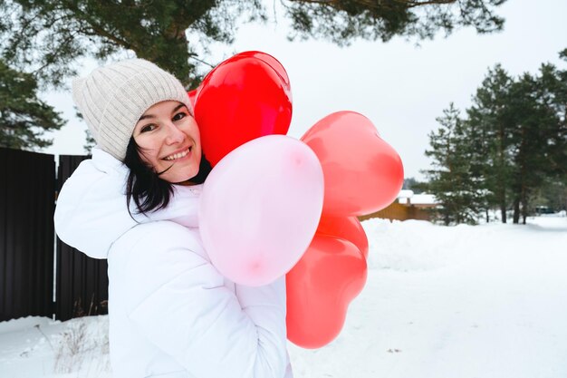 雪と冬の屋外でハート型の風船を持つ幸せな女性。バレンタインデー、愛と夢中、彼氏からの贈り物、愛の宣言、ライフスタイル