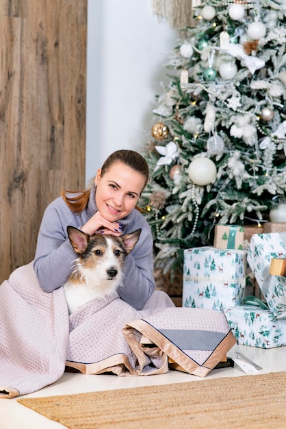 Happy woman with her dog greets merry christmas and new year the female sits with her pet by the chr...