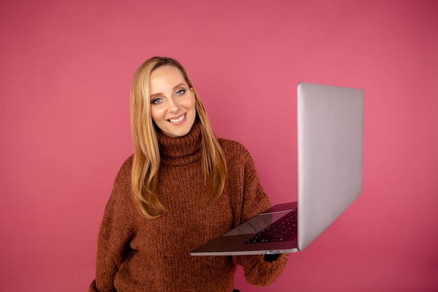 Happy woman with laptop isolated in the pink studio.