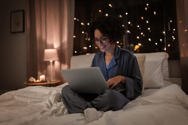 happy woman with laptop working in bed at night