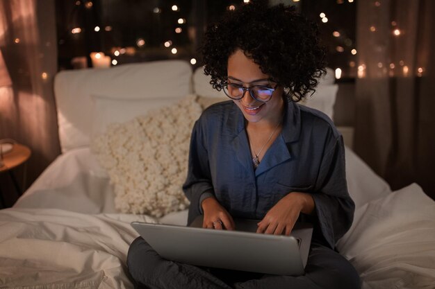 happy woman with laptop working in bed at night