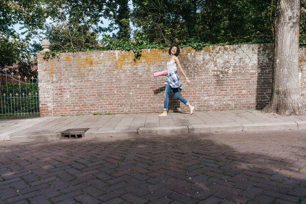 Happy woman with mat walking on pavement