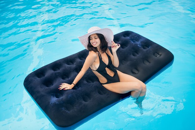 Счастливая женщина с идеальной фигурой лежит на матрасе в бассейне