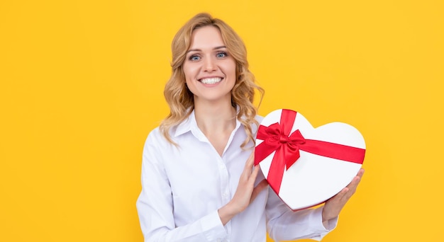 Happy woman with present heart box on yellow background