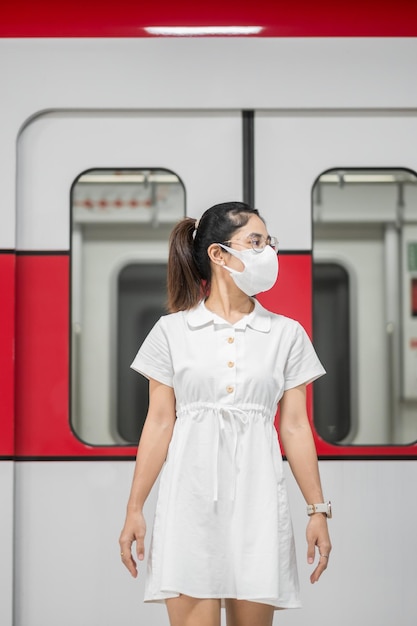 Happy woman with Protective face mask prevention coronavirus inflection during waiting train. public transportation. social distancing, new normal and safety under covid-19 pandemic