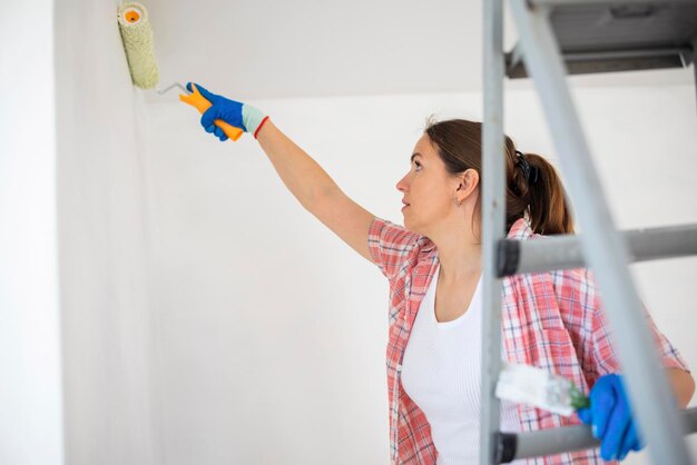 Photo happy woman with roller painting wall in her new apartment