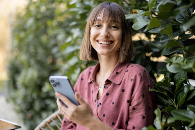 Happy woman with smart phone on natural background outdoors