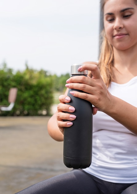 Happy woman working out on the sports ground in sunny summer day, drinking water from the bottle