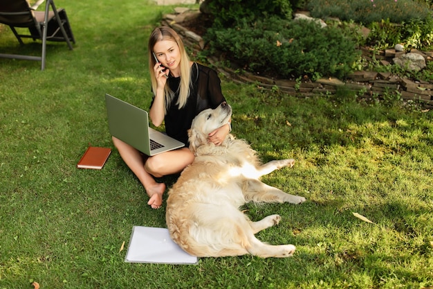 Foto donna felice che lavora con il computer portatile e gioca con il cane labrador all'aperto