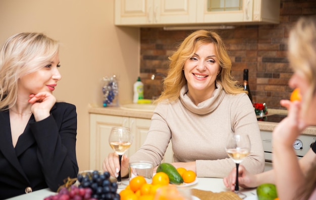 Donne felici in abiti da sera nella cucina di casa si sono riunite al tavolo festivo