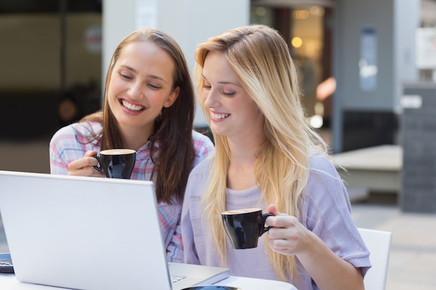 Happy women friends drinking coffee and looking at laptop