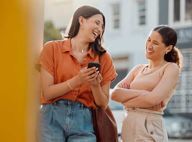 Foto amici di donne felici che parlano divertendosi e ridono mentre leggono un testo su un telefono insieme fuori giovani femmine spensierate e rilassate che chiacchierano godendo di una conversazione e del tempo libero in centro