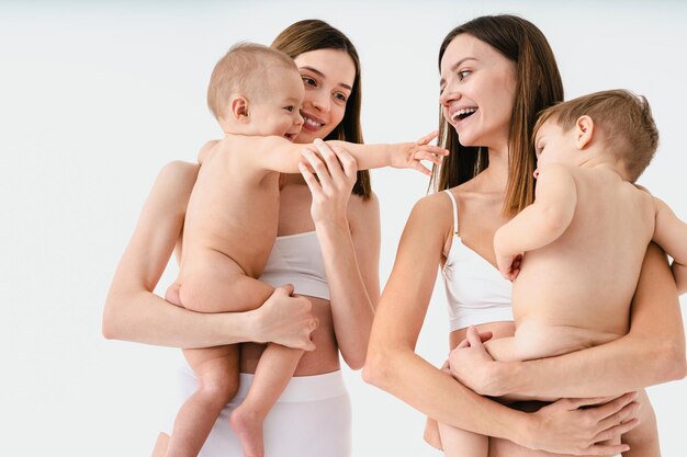 Happy women holding their babies on colored background -  Young women wearing underwear taking care of their little sons  - Pregnancy, motherhood, people and expectation concept