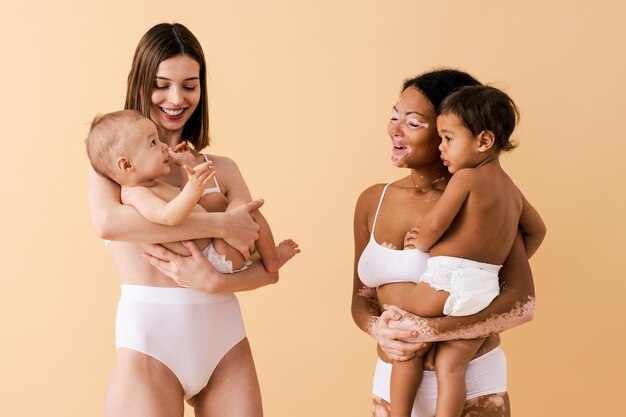 Happy women holding their babies on colored background -  Young women wearing underwear taking care of their little sons  - Pregnancy, motherhood, people and expectation concept