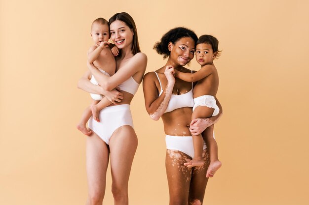 大きなお腹を持つ幸せな妊婦とスタジオで赤ちゃんを持つ美しい母親-妊娠中の女性と下着を着ている子供を持つお母さんの多民族グループ-妊娠、母性、人々、体の位置