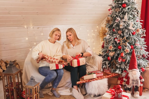 Happy women mothers are preparing for Christmas, New year pack gifts at home while sitting near Christmas tree. Winter holidays, home decoration concept