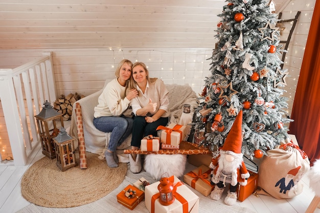 Happy women mothers are preparing for Christmas, New year pack gifts at home while sitting near Christmas tree. Winter holidays, home decoration concept