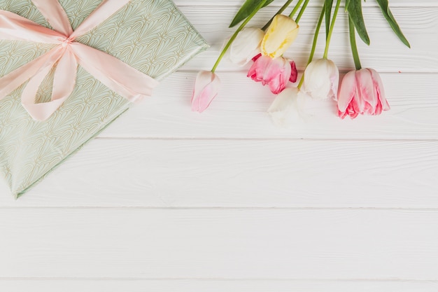 Happy Women's day. Tulips bouquet and a gift box on white wooden background.