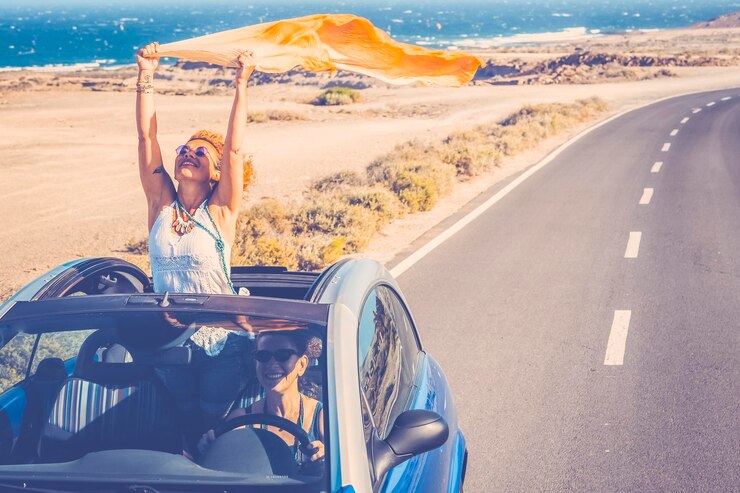 Photo 幸せな女性旅行者は、コンバーチブル車でロードトリップを楽しむ 屋根の外に一人の女性が楽しむ 風光明媚な砂漠の目的地 車の運転 旅行中の車で興奮した友人のカップル 冒険