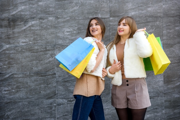 Happy women with shopping bags in fur coats posing on city street