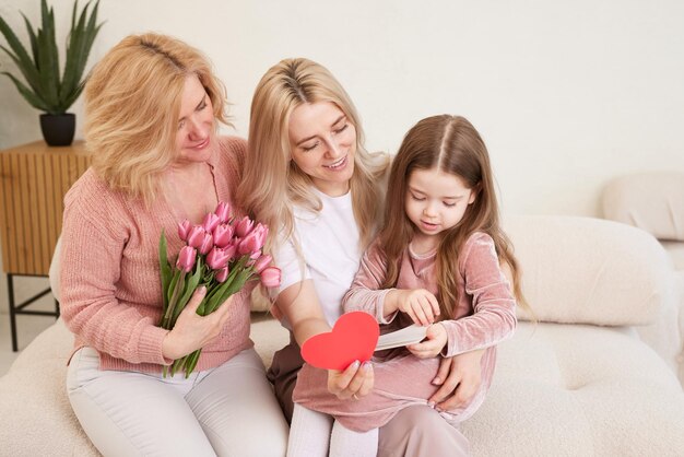 Happy Womens Day The childs daughter congratulates her mother and grandmother giving them flowers tulips Grandmother mother and girl smile and hug Family holiday and unity