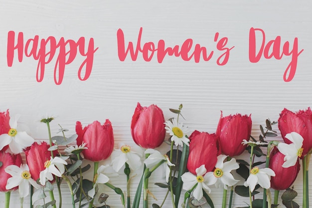 Photo happy womens day text on beautiful red tulips daffodils eucalyptus flowers border on rustic white wood flat lay modern greeting card stylish handwritten sign international women's day