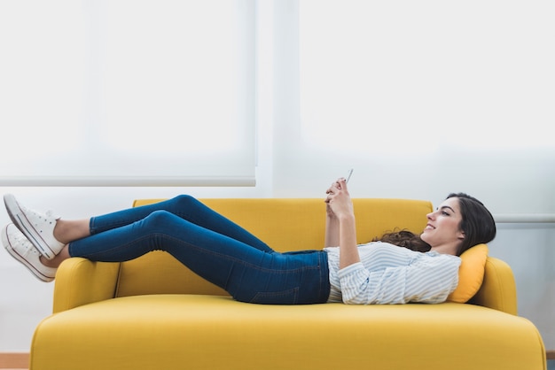 Photo happy worker lying on the couch and using her cell phone