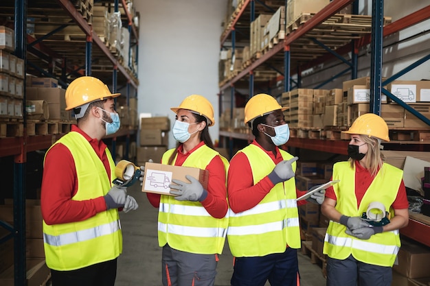 Happy workers talking inside warehouse while wearing safety masks during coronavirus outbreak - Focus center faces