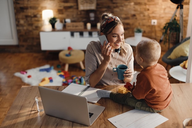 Photo happy working mother making a phone call while being with her son at home