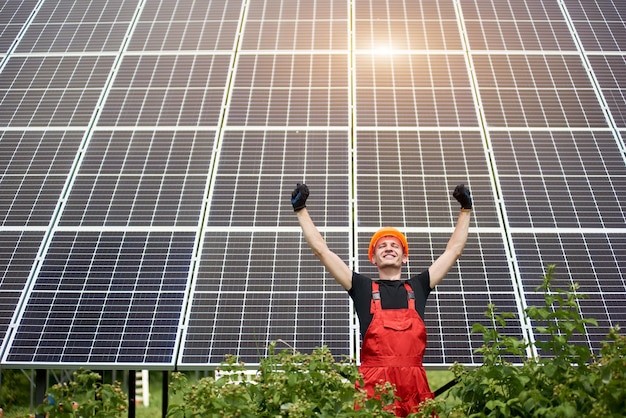 Счастливая работающая солнечная станция, поднимающая руки на фоне фотоэлектрических панелей