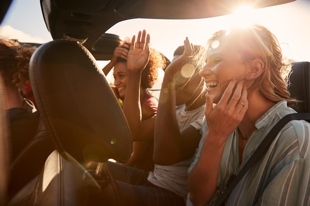 Happy young adult friends on a road trip vacation travelling in the back of an open car