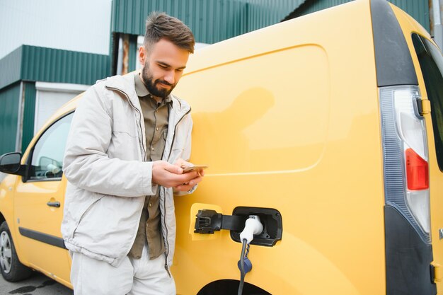 小さな公共の駅から自動車のバッテリーを充電する幸せな若い成人男性