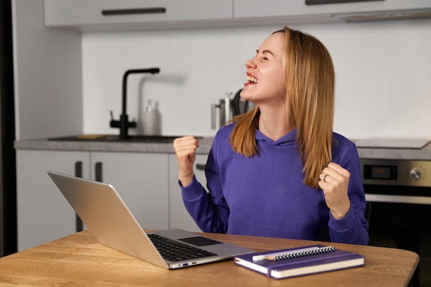 自宅のコンセプトからラップトップの仕事を使用してキッチンで幸せな若い大人の女性の仕事の研究