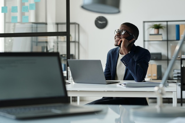 Happy young African American broker talking to client on smartphone in office