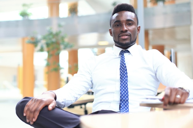 Happy young African-American businessman looking at camera at workplace in office.