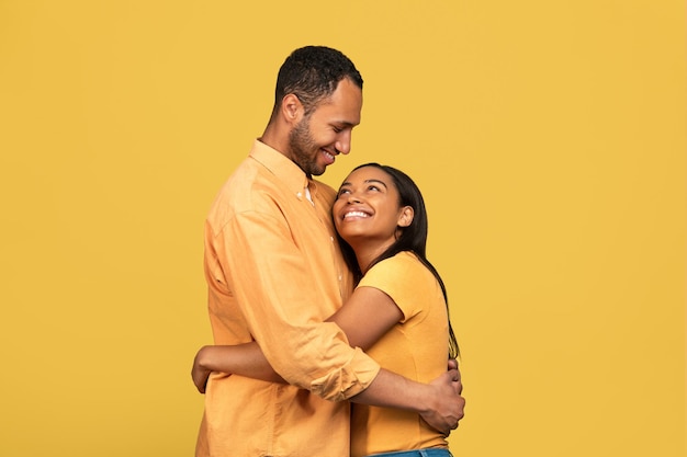 캐주얼 옷을 입은 행복한 젊은 아프리카계 미국인 커플이 노란색으로 서로를 껴안고 바라보고 있습니다.
