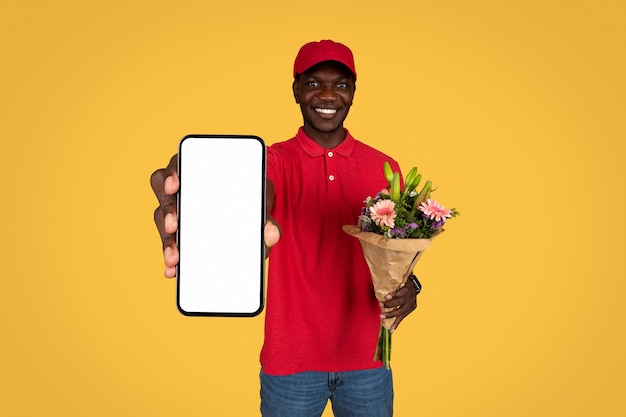 Happy young african american delivery man in uniform show smartphone bouquet flowers