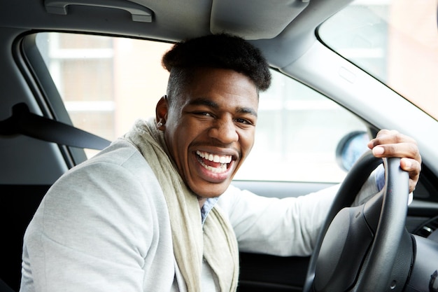 Счастливый молодой афроамериканец сидит в машине и смеется.