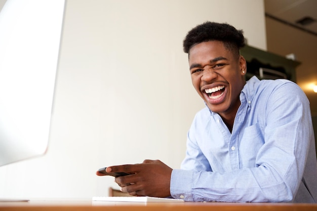 happy young african american man sitting with cellphone at computer desk