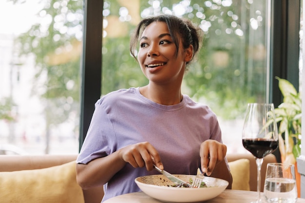 happy young african american woman eating salad and drinking wine in restaurant