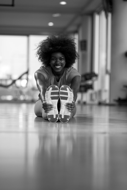 Photo happy young african american woman in a gym stretching and warming up before workout